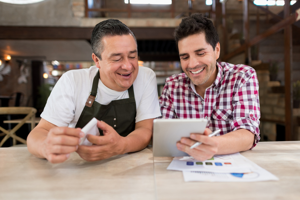 Two male restaurant owners using computer software to ensure their business records are kept safely - adhering to New York restaurant payroll practices.
