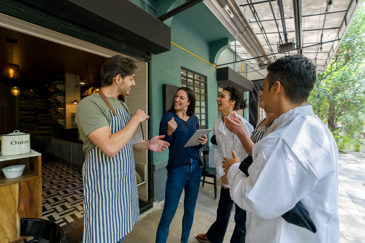 Restaurant owners managing restaurant payroll and other benefits to motivate their employees - having a team meeting outside.